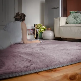 Eine Frau liegt gemütlich auf einem Hochflor Teppich und liest - Eine Frau liegt gemütlich auf einem Hochflor Teppich und liest