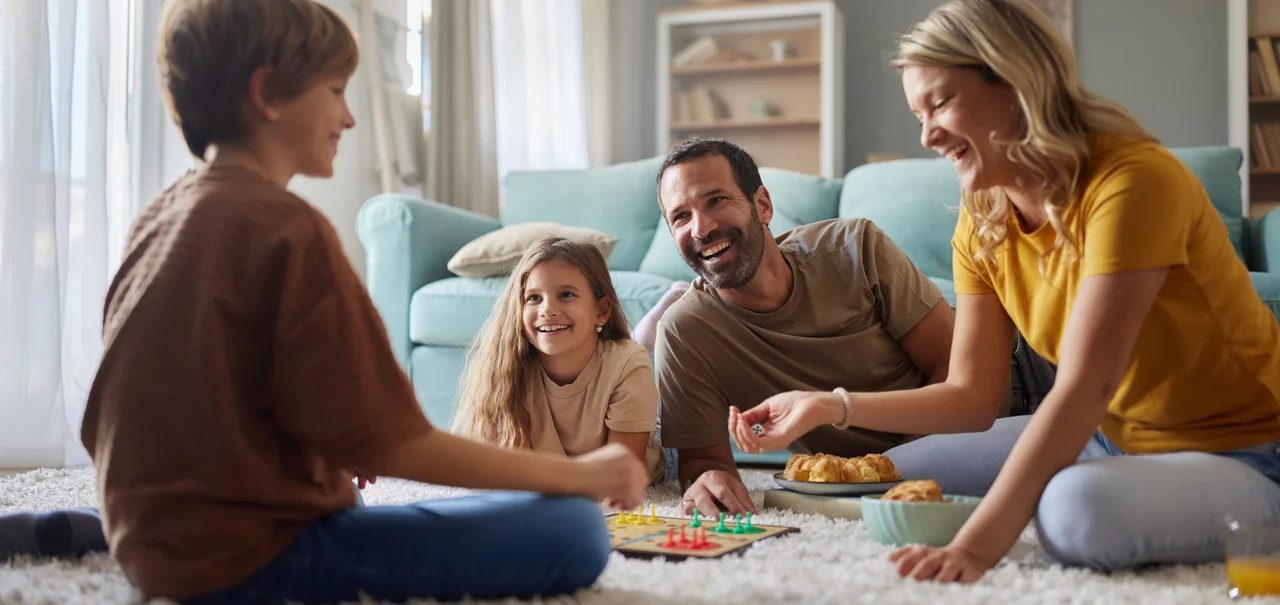 Glückliche Eltern und ihre Kinder, die zu Hause im Wohnzimmer auf Hochflor-Teppich spielen. - Glückliche Eltern und ihre Kinder, die zu Hause im Wohnzimmer auf Hochflor-Teppich spielen.